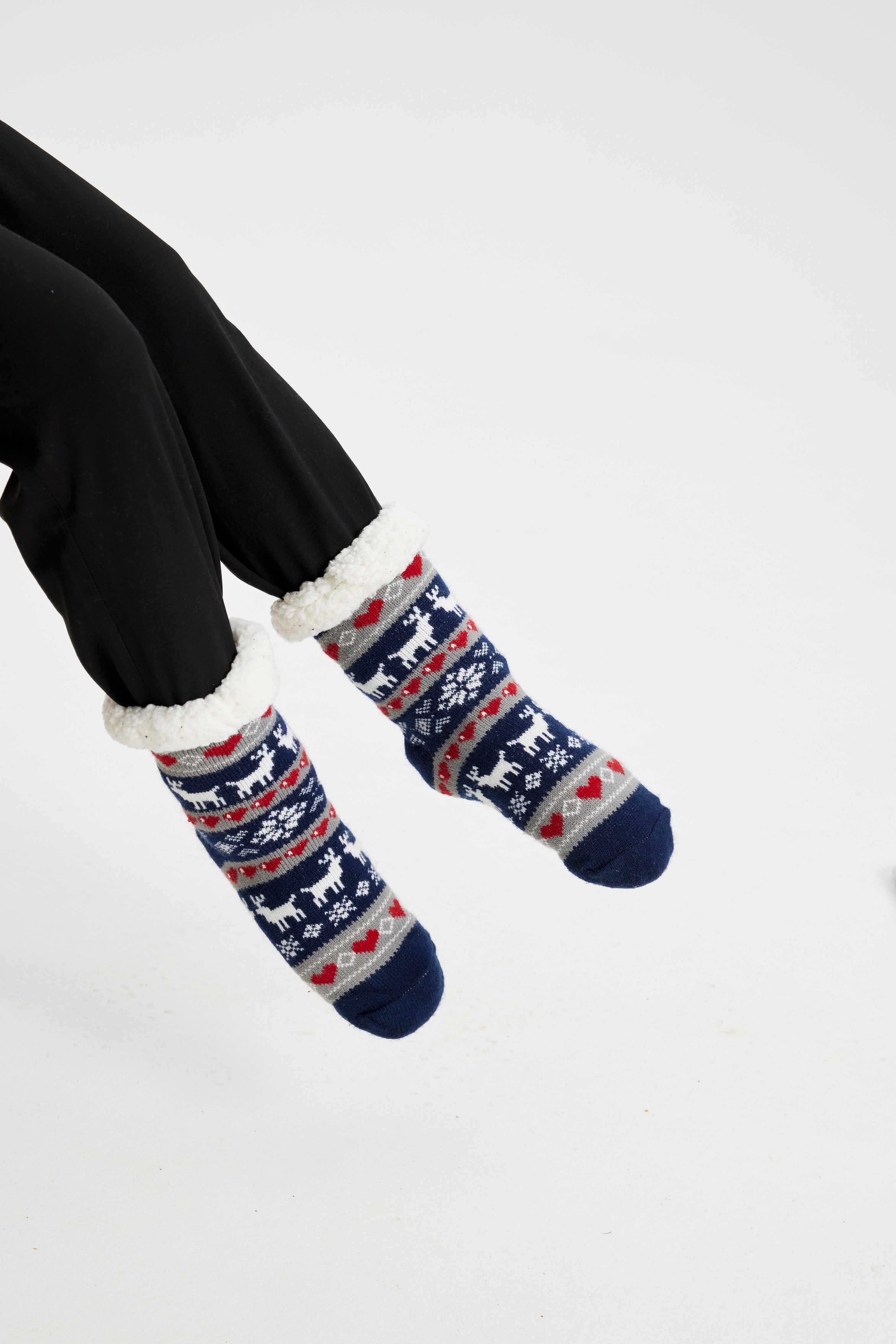 Une paire de pieds portant des chaussettes de Noël bleues ornées de rennes et de cœurs.
